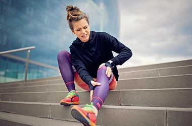 A runner sitting on stone steps and holding her leg in pain after an injury
